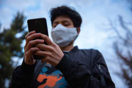 Young latin man with mask is using his phone in the streetの写真素材
