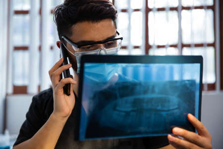Dentist Examining a Radiography at her clinic office. He speaks on the phoneの写真素材