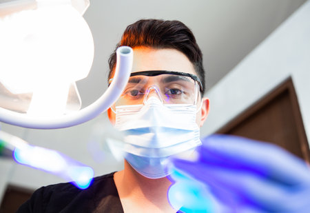 Focus on the instruments of a dentist wearing glasses and maskの写真素材