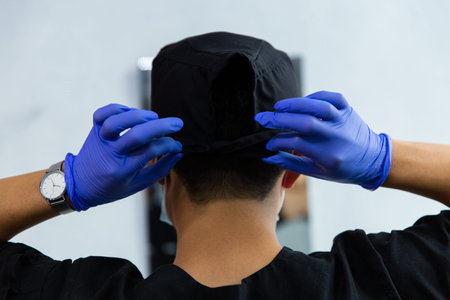 Doctor wears blue latex gloves to put on a cap. Back view
