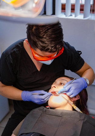 Close-up of a dentist wearing protective orange glasses. The patient receives a tooth whitening...