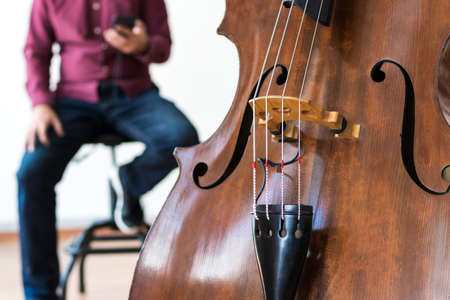 Close-up of a double bass. Behind there is a man with his phone. White backgroundの写真素材