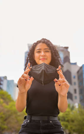 Young woman with curly head putting a black mask on her faceの写真素材