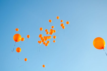 Orange balloons rising to the sky, balloons released against blue skyの写真素材