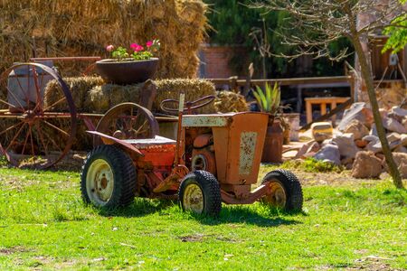 A old red tractor sits under a tree on the edge of a farm field.の写真素材