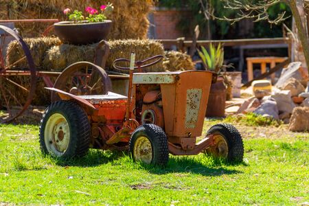 A old red tractor sits under a tree on the edge of a farm field.の写真素材