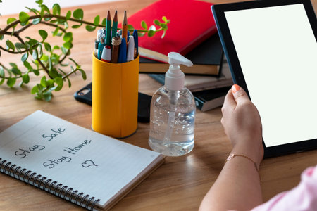 Women's hands working at home, with a tablet and a stay safe sign, stay home. antibacterial gel,...