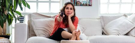 Real woman bored of watching television at home. Covid 19 coronavirus quarantine. Stay homeの写真素材