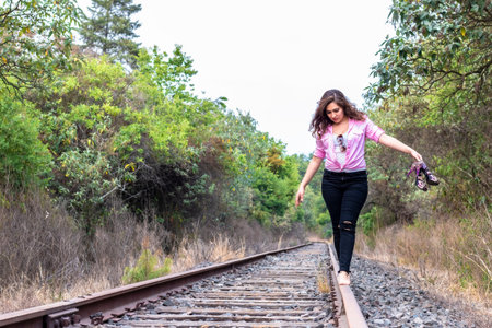 casual young man in pink shirt, black pants and heels walking on a railwayの写真素材