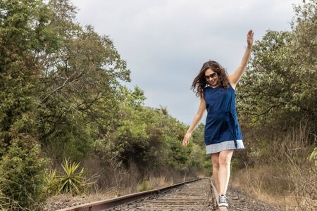 casual young woman in blue dress walking on a railwayの写真素材