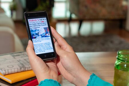 Online news on a mobile phone. Close up of the page of a businesswoman reading news or articles on a smartphone screen application. Smartphone with hand. Mockup website. Newspaper and Internet portal.の写真素材