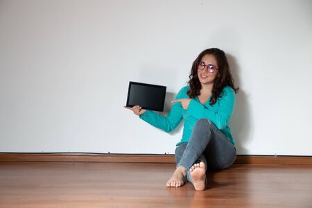 Real woman sitting on the floor of an empty room, pointing at a tablet and drinking a glass of wine. Copy spaceの写真素材