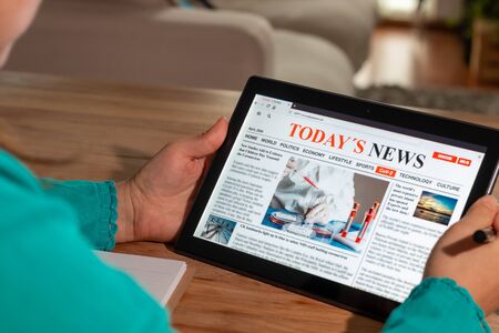 Woman reading the news on a tablet at home. Imaginary online, mobile website, application or news portal on modern touch screen. Take notes in a notebookの写真素材