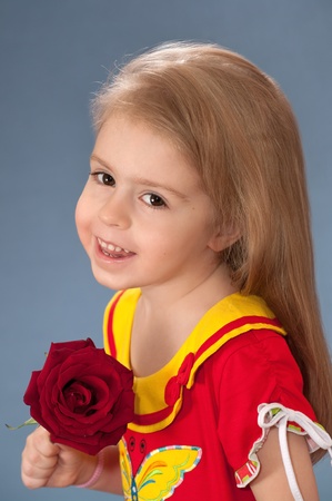 The little girl with a red rose. The three-year cheerful child.の写真素材