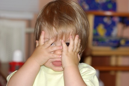 Ð¡hild hamming. A little girl hides her face in her hands and shows the languageの写真素材