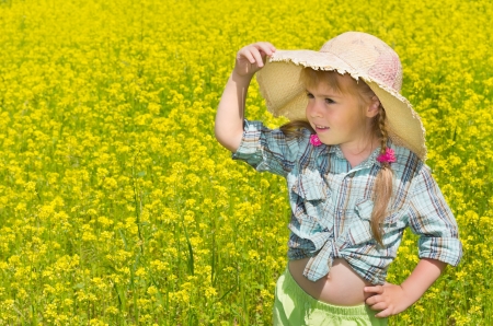 The little girl in the hat among the blossoming of the field. The child looks into the distance.の写真素材