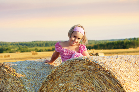 Cheerful little girl in  field on straw rollsの写真素材