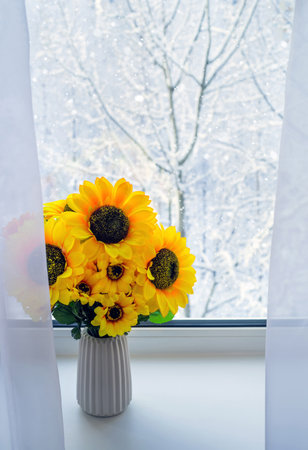 Sunflowers in the winter season on window. Snow-covered trees outside the window. Bright sunflowers against the backdrop of winter landscape.の写真素材