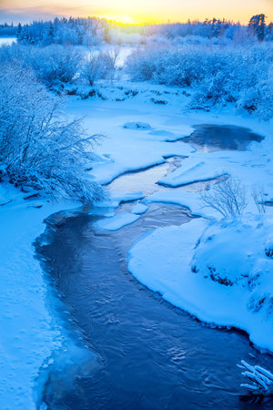 Winter frosty landscape. Landscape with river and snowy forest in Western Siberia. Freezing river against sunset background. Frosty winter evening.の写真素材