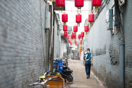 Pingyao, China - 08 14 2016: A chinese man walking in a street with red lanterns in Pingyao. The ancient city of Pingyao is a famous tourism destination. Shanxi, Chinaのeditorial素材