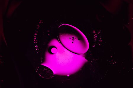 magenta oil droplets from a mixture of water and olive oil illuminated with colored bulb with dark backgroundの写真素材