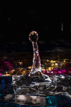 water drops splash forming ripples and waves and abstract water columns in a colorful backgroundの写真素材