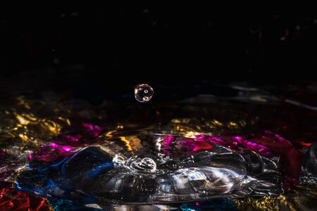 water drops splash forming ripples and waves and abstract water columns in a colorful backgroundの写真素材