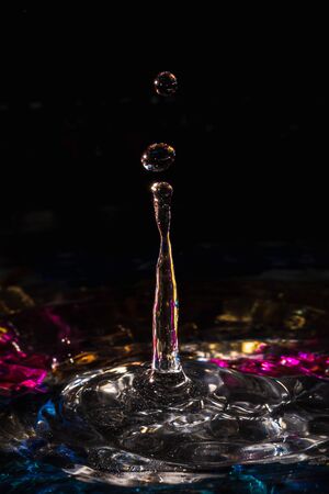 water drops splash forming ripples and waves and abstract water columns in a colorful backgroundの写真素材