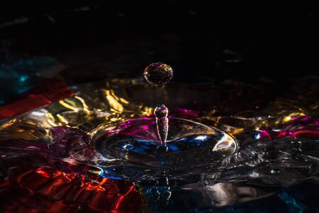 water drops splash forming ripples and waves and abstract water columns in a colorful backgroundの写真素材