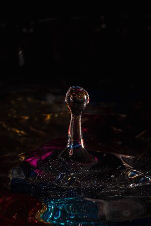 water drops splash forming ripples and waves and abstract water columns in a colorful backgroundの写真素材