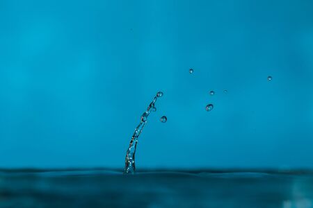 water drops splash forming ripples and waves and abstract water columns in light blue backgroundの写真素材