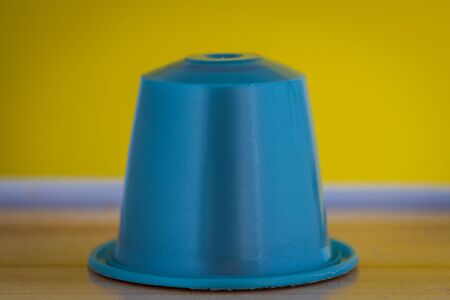 closeup lateral view of an aromatic, tasty espresso light blue coffee capsule with yellow backgroundのeditorial素材