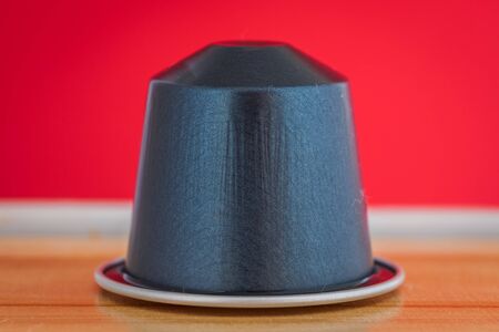 closeup lateral view of an aromatic, tasty espresso dark blue coffee capsule with red backgroundのeditorial素材