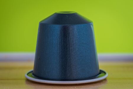 closeup lateral view of an aromatic, tasty espresso dark blue coffee capsule with lemon green backgroundのeditorial素材
