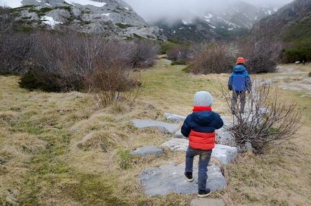two little kids hiking in the mountains during the winter ending and the spring beginning in a cold cloudy dayの写真素材