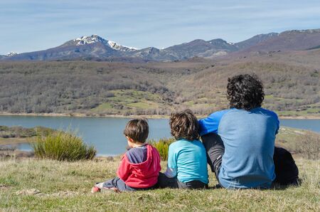 father and his two sons relaxing for a moment and enjoying the views after a hard hiking in the mountainsの写真素材