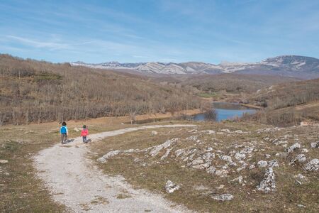 two little kids hiking in the mountains during the winter ending and the spring beginning in a warm sunny dayの写真素材