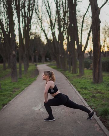 young blonde girl with blue eyes and black outfit doing outdoors exercises in a park on a warm winter afternoonの写真素材