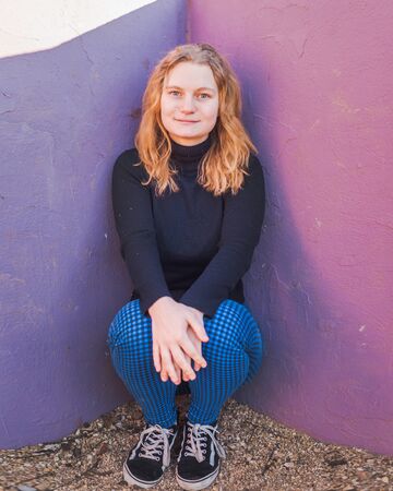 blonde girl with blue eyes with purple wall as background in a park in a winter sunny afternoonの写真素材