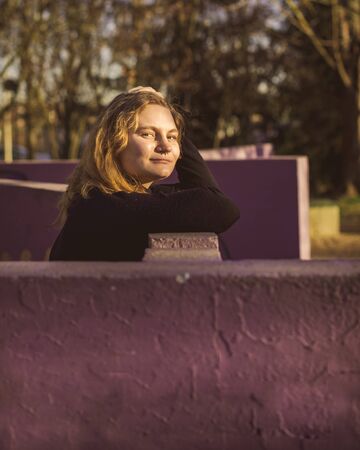 blonde girl with blue eyes with purple wall as background in a park in a winter sunny afternoonの写真素材