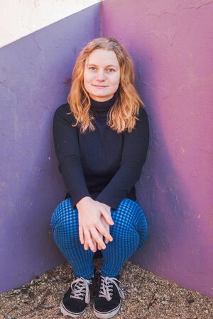 blonde girl with blue eyes with purple wall as background in a park in a winter sunny afternoonの写真素材