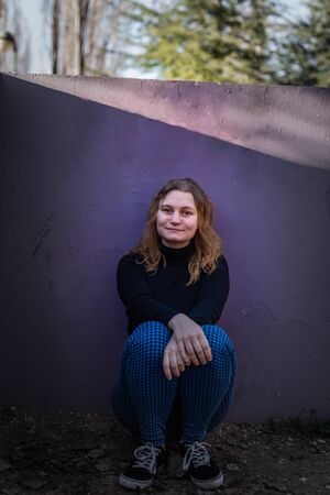 blonde girl with blue eyes with purple wall as background in a park in a winter sunny afternoonの写真素材