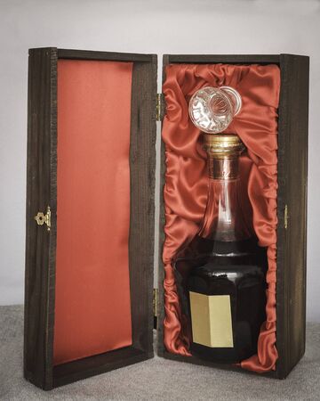 dark liquor in fancy crystal bottle packaged in elegant oak wood box with red clothの写真素材