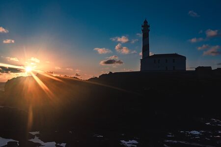lighthouse with sunbursts during dawn in a winter day with cloudy sky in Menorca, Spainの写真素材