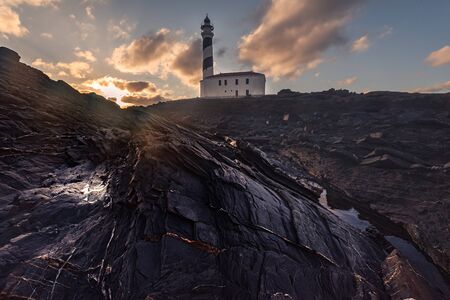 lighthouse with stony foreground during dawn in a winter day with cloudy sky in Menorca, Spainの写真素材