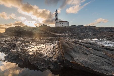 lighthouse with stony foreground during dawn in a winter day with cloudy sky in Menorca, Spainの写真素材