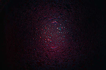 red, blue and purple oil droplets illuminated with colored bulb with dark background. Water and olive oil mixture.の写真素材