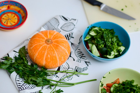 vegetarian food and healthy eating concept - close up of fresh ripe sliced cucumber in a plate, pumpkin and parsley on white tableの写真素材