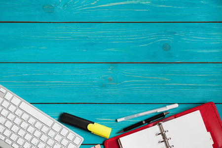 Wooden blue turquoise background desk with a laptop, red notebook and penの写真素材