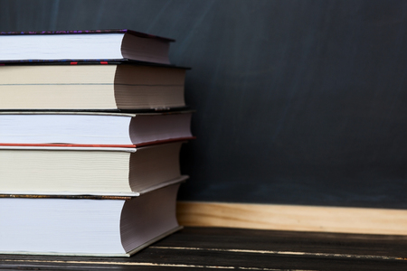 School concept. Stack of books close up on wooden desk with chalkboard as backgroundの写真素材